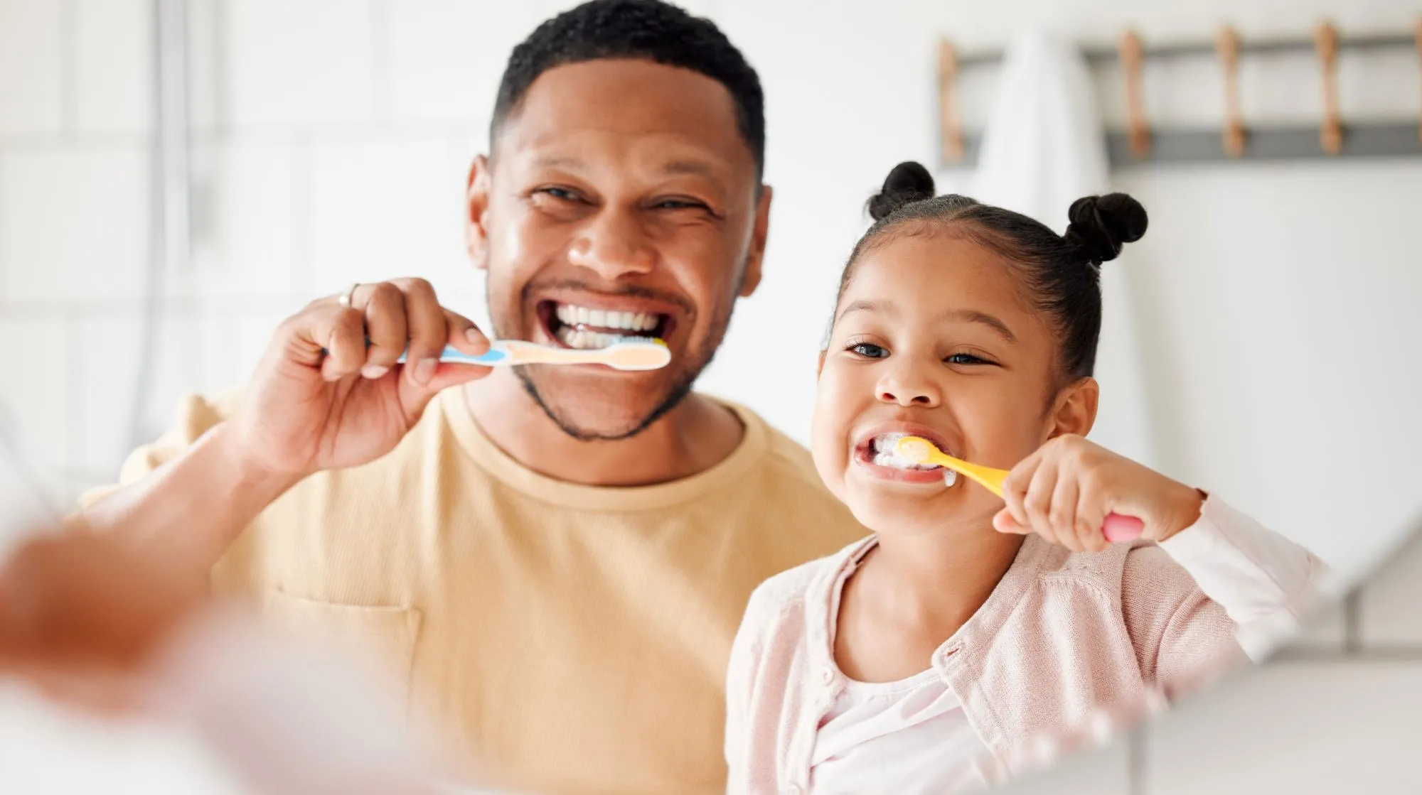 A smiling father and daughter brushing their teeth