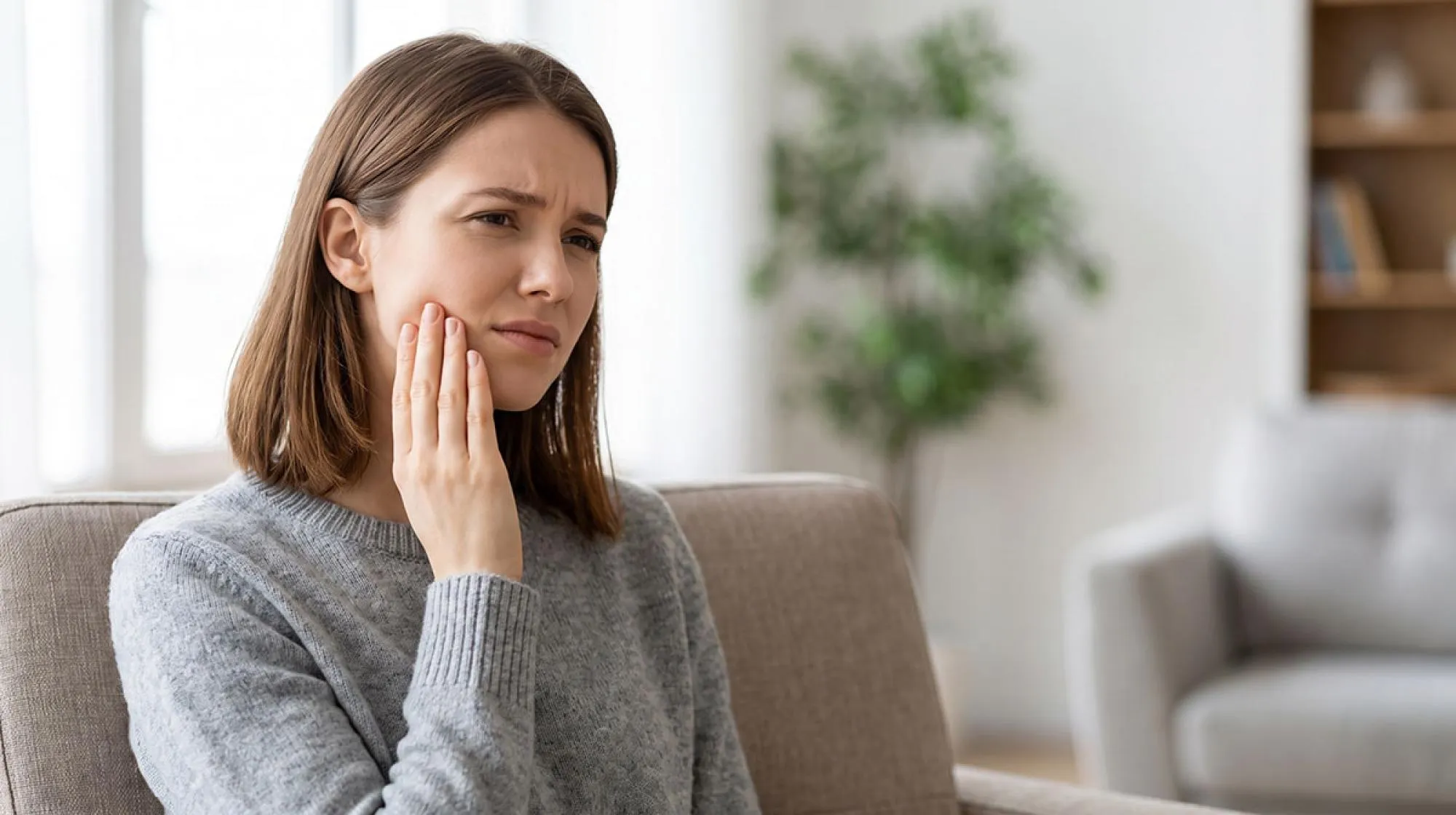 A woman holding her cheek due to a severe, sudden toothache requiring emergency dental care