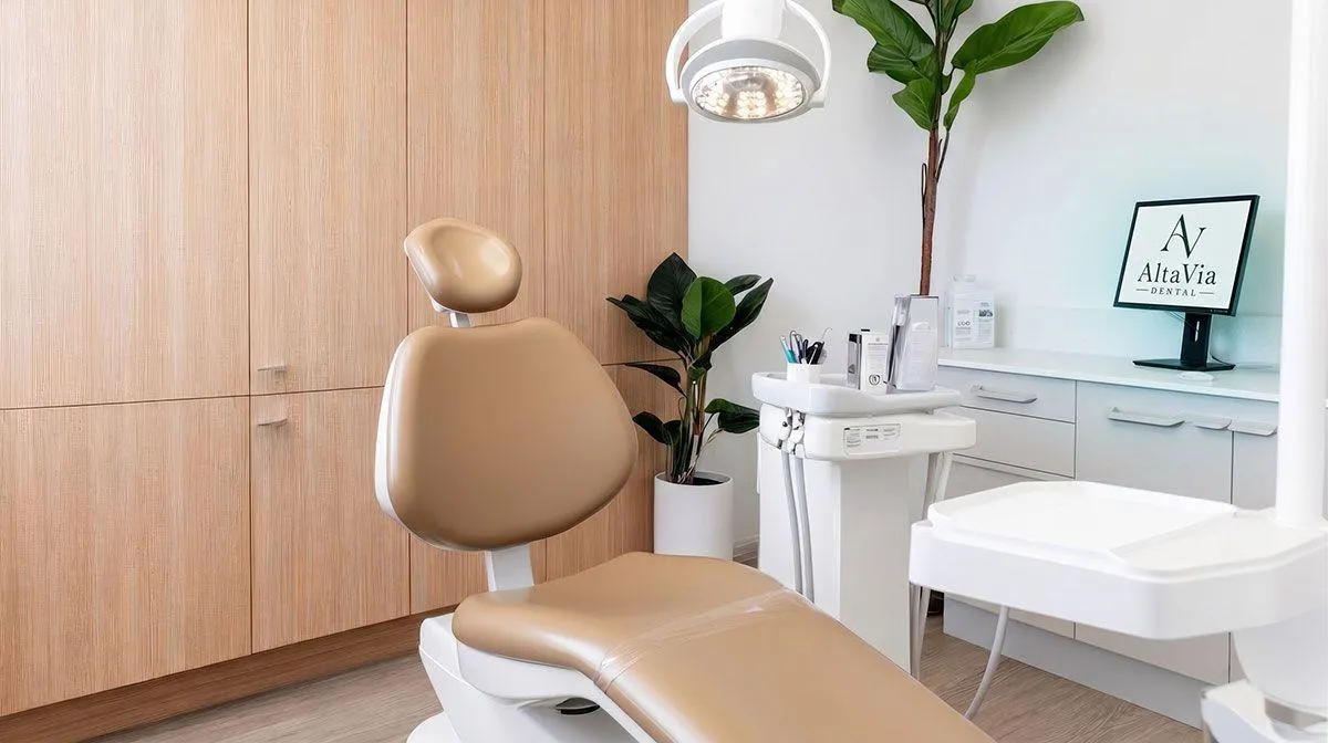 A bright AltaVia treatment room with oak cabinetry, a soft tan dental chair and leafy plants